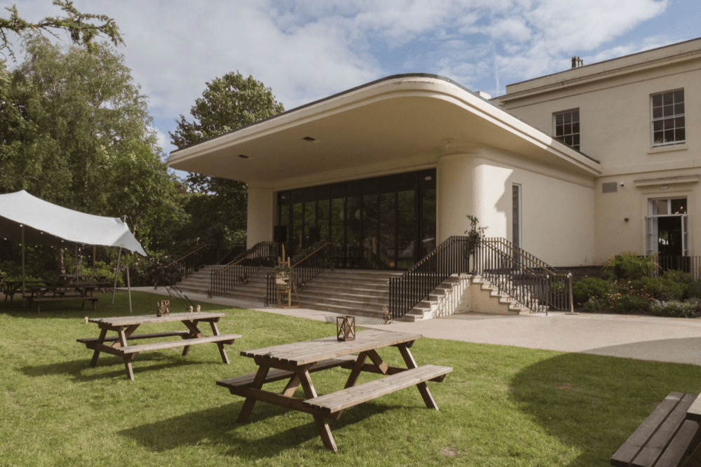 The Mansion House Garden with an Art Deco stage. At the back of the Mansion one can see the bi fold doors into the theatre room and there are picnic benches on the lawn