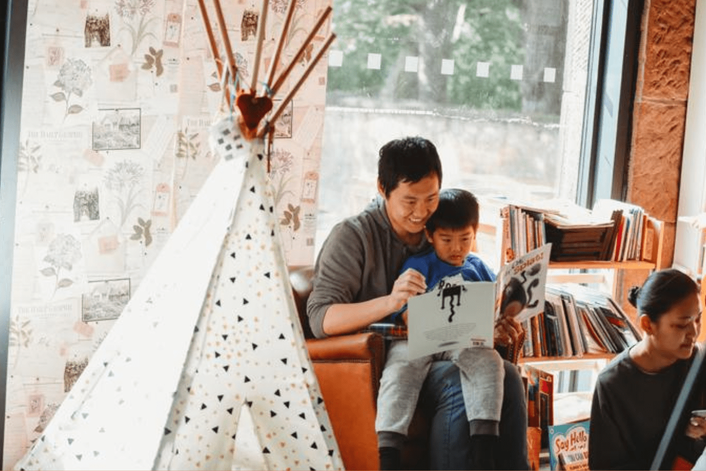 little boy sat on the lap of his carer smiling and reading