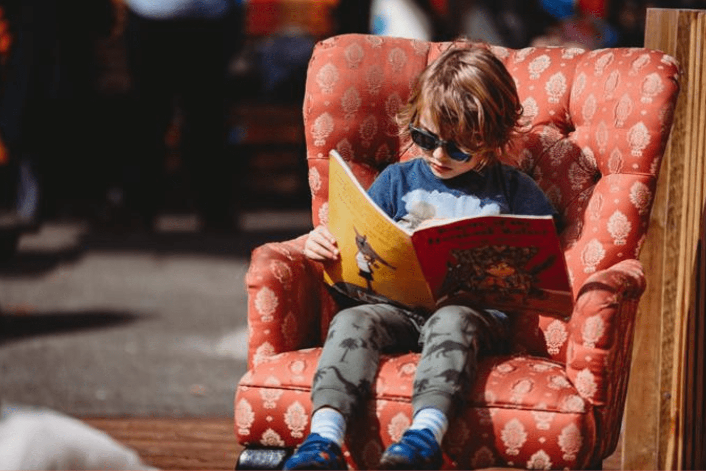 little boy in sunglasses sat in oversized armchair reading