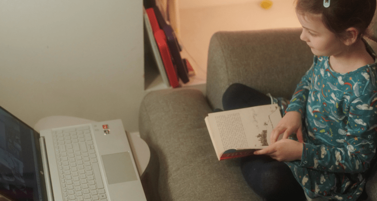 Little girl reading in front of a laptop with a volunteer online