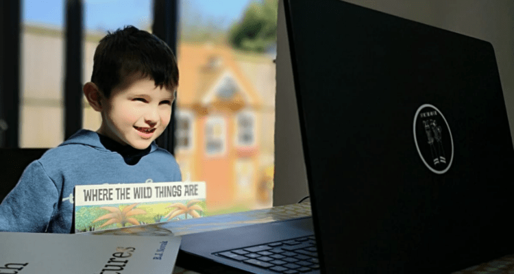 Little boy reading with a smile in front of a laptop for their volunteer