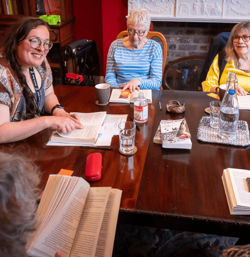 Reader Leader smiling and pointing at book while two group members smile and look over to her