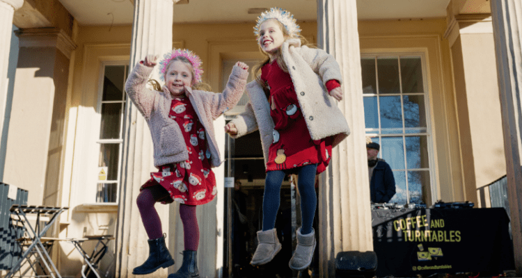 Two children jumping for joy outside Calderstones Mansion House Liverpool in their Christmas outfits